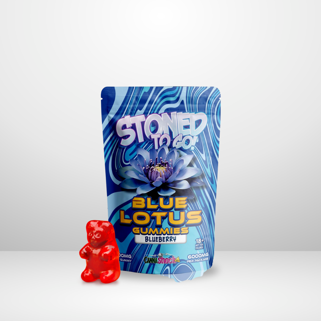 En förpackning märkt Cannashock Blå Lotus Godis 6000 mg står upprätt bredvid en enda röd gummibjörn på en vanlig vit yta med ljusgrå bakgrund.