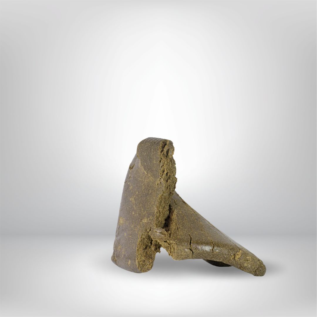 En 5 g stor bit av Partybolagets Dark Charas THCA Hash (31%), solid och brun med grova kanter, står upprätt mot en vanlig ljusgrå bakgrund.