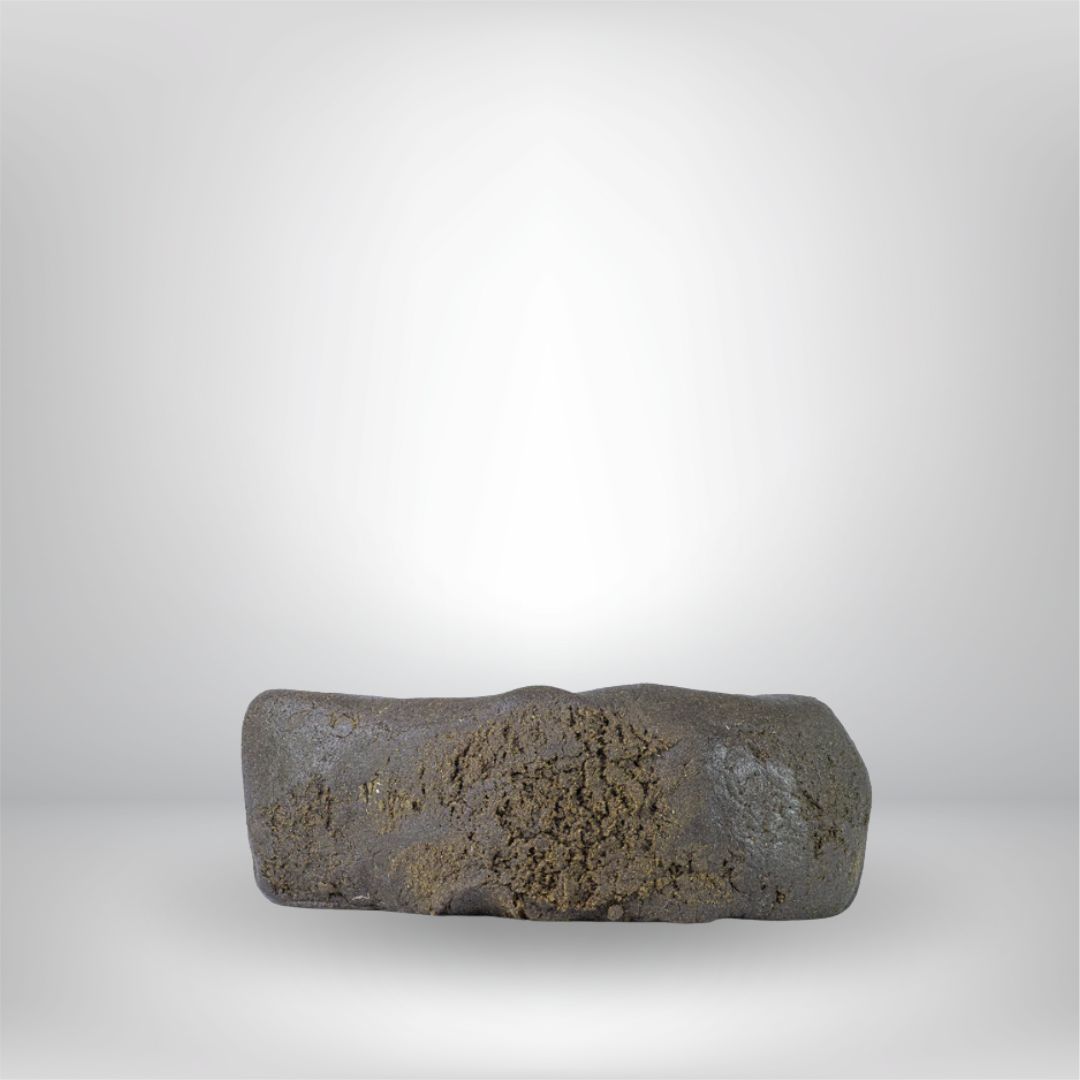 En ungefär rektangulär, mörkbrun Light Charas THCA 5g 30% - Hash från Partybolaget med en ojämn, strukturerad yta, mot en vit bakgrund med dämpad belysning. Premiumhantverk och lagligt i Sverige.